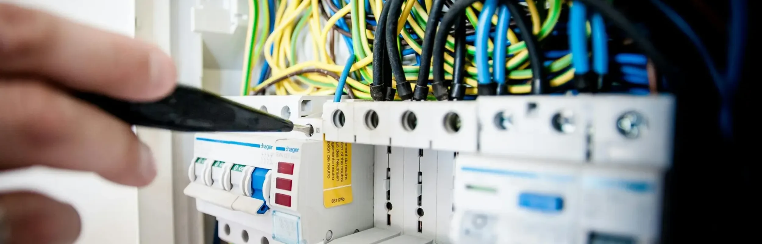 Hand of electrician working on a circuit breaker panel with colorful wires, ensuring safe electrical connections.